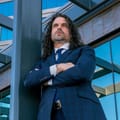 Brian Lee Nash in a navy plaid suit with arms crossed, standing in front of a glass building